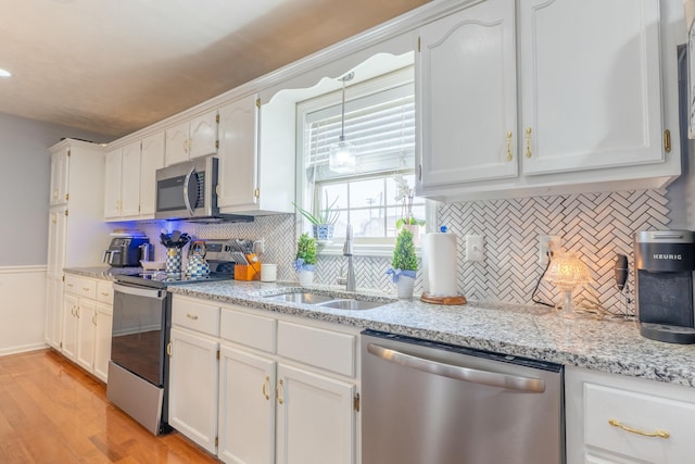 kitchen featuring light wood-style flooring, a sink, stainless steel appliances, white cabinetry, and backsplash