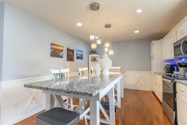 kitchen with a wainscoted wall, a breakfast bar area, appliances with stainless steel finishes, wood finished floors, and white cabinets