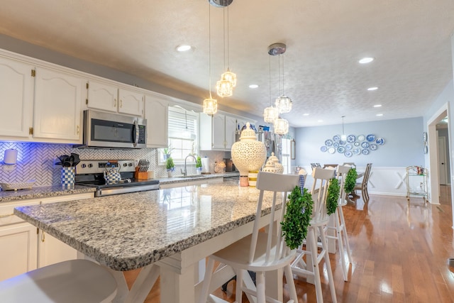 kitchen featuring wood finished floors, a breakfast bar, appliances with stainless steel finishes, backsplash, and a center island