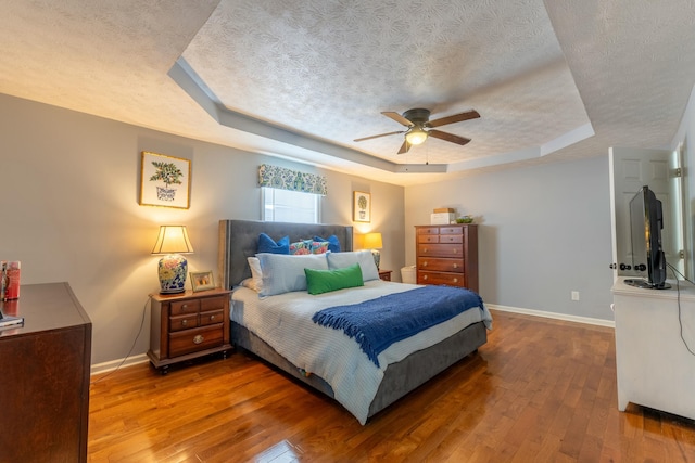 bedroom with hardwood / wood-style floors, a tray ceiling, baseboards, and a textured ceiling