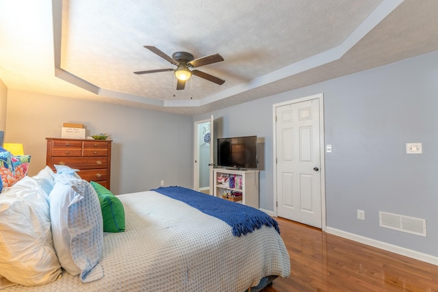 bedroom with wood finished floors, baseboards, visible vents, a textured ceiling, and a raised ceiling