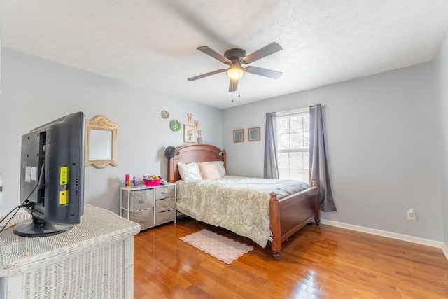 bedroom with a textured ceiling, light wood-type flooring, baseboards, and a ceiling fan