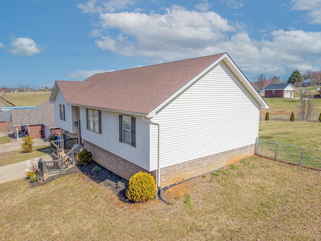 view of side of property featuring a lawn, a shingled roof, and fence