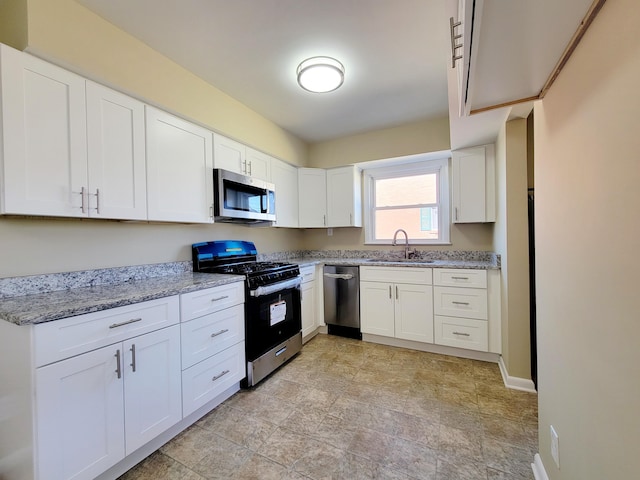 kitchen featuring baseboards, light stone countertops, stainless steel appliances, white cabinetry, and a sink