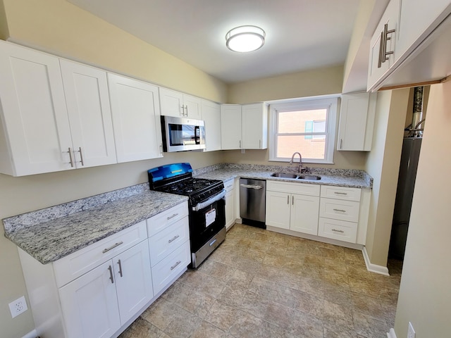 kitchen with light stone counters, baseboards, a sink, stainless steel appliances, and white cabinetry