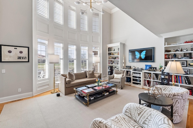 living room featuring built in features, wood finished floors, baseboards, a towering ceiling, and crown molding