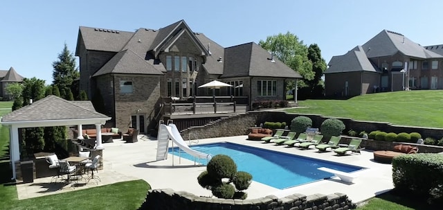 rear view of property featuring stone siding, a patio, a yard, an outdoor pool, and stairs