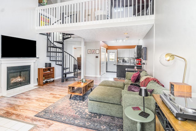 living area with baseboards, a fireplace with flush hearth, stairs, light wood-style floors, and a towering ceiling