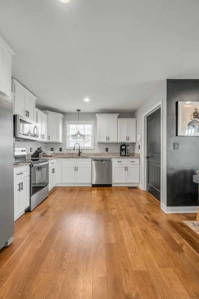 kitchen with stainless steel appliances, white cabinetry, light stone countertops, and light wood finished floors