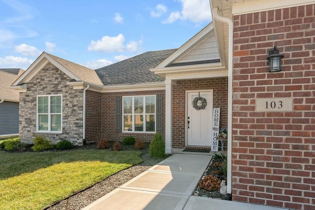 view of exterior entry featuring a yard, brick siding, stone siding, and a shingled roof