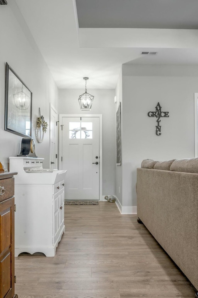 foyer entrance featuring a chandelier, visible vents, baseboards, and light wood-style floors