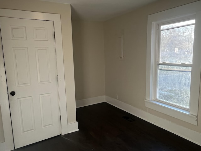 spare room featuring dark wood finished floors, visible vents, a healthy amount of sunlight, and baseboards