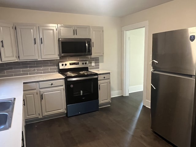 kitchen featuring baseboards, light countertops, decorative backsplash, dark wood-style floors, and stainless steel appliances