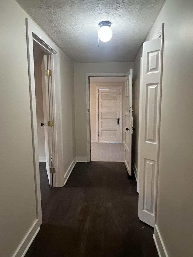 hall featuring baseboards, a textured ceiling, and dark wood-style flooring