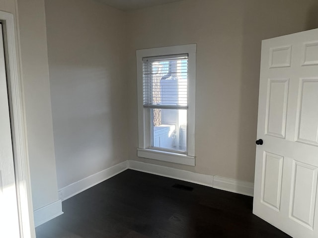 empty room with dark wood-type flooring, visible vents, and baseboards