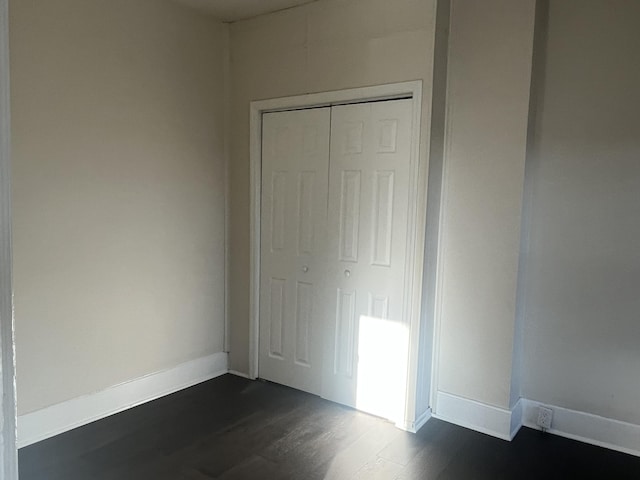 unfurnished bedroom featuring a closet, baseboards, and dark wood-style flooring