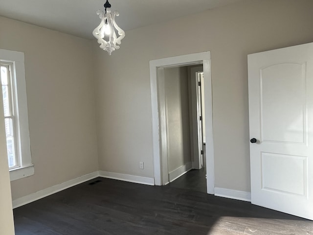 empty room featuring a chandelier, visible vents, dark wood-type flooring, and baseboards