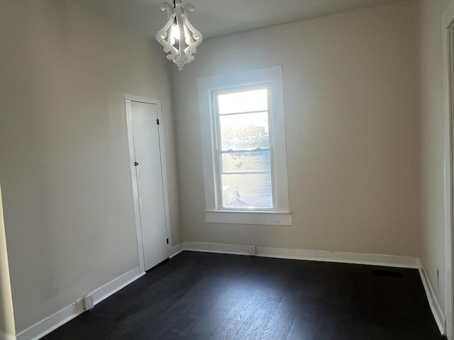 empty room with a chandelier, visible vents, dark wood-type flooring, and baseboards