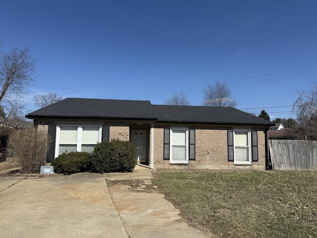 ranch-style home with a front yard, fence, brick siding, and roof with shingles