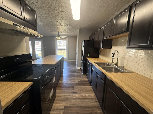 kitchen featuring black appliances, a sink, dark wood finished floors, butcher block counters, and decorative backsplash