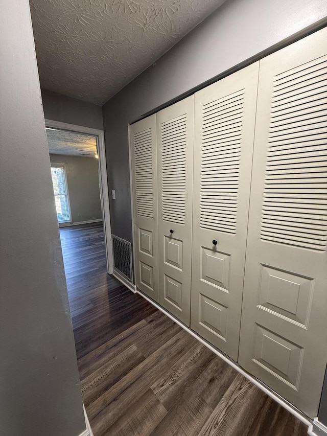 hall featuring baseboards, visible vents, dark wood-style flooring, and a textured ceiling