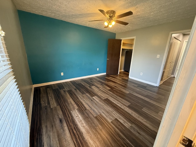 unfurnished bedroom featuring baseboards, ceiling fan, dark wood-type flooring, a textured ceiling, and a walk in closet