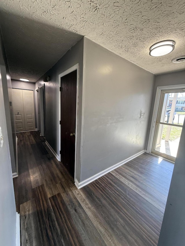 corridor featuring visible vents, a textured ceiling, dark wood-type flooring, and baseboards