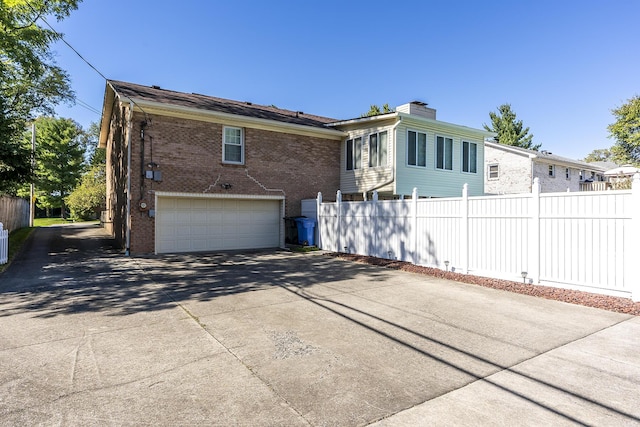 exterior space featuring brick siding, driveway, a garage, and fence