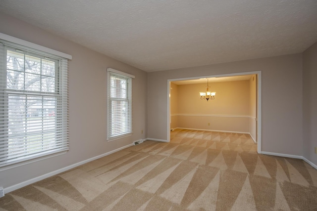 unfurnished room with visible vents, light carpet, a textured ceiling, an inviting chandelier, and baseboards