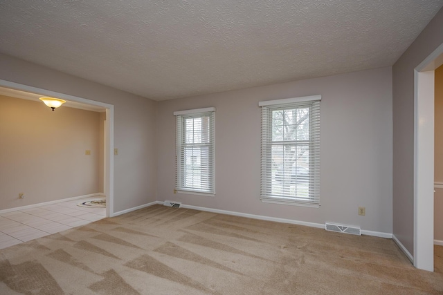 empty room with baseboards, visible vents, carpet floors, tile patterned flooring, and a textured ceiling