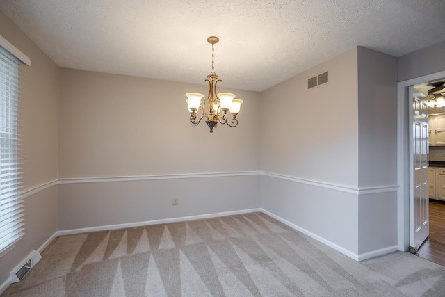 spare room with visible vents, light carpet, a notable chandelier, and baseboards