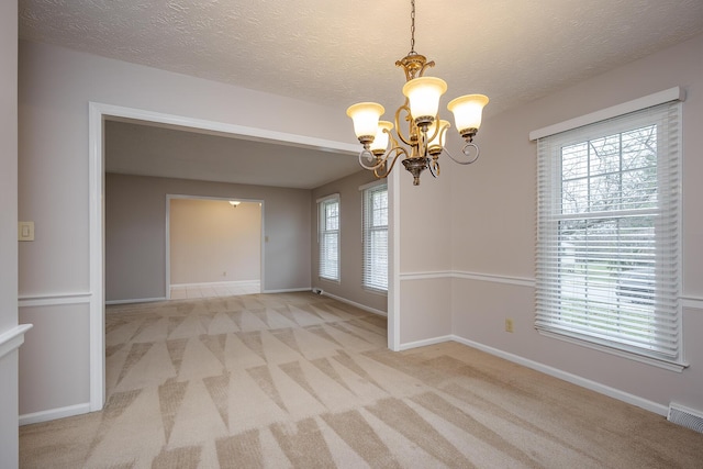 spare room with a notable chandelier, light colored carpet, a textured ceiling, and baseboards