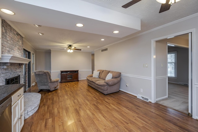 living area featuring a fireplace, visible vents, light wood finished floors, and a textured ceiling