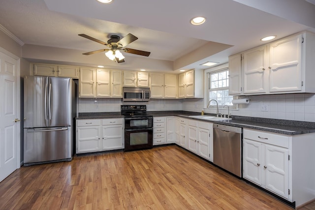 kitchen with wood finished floors, a sink, stainless steel appliances, dark countertops, and backsplash