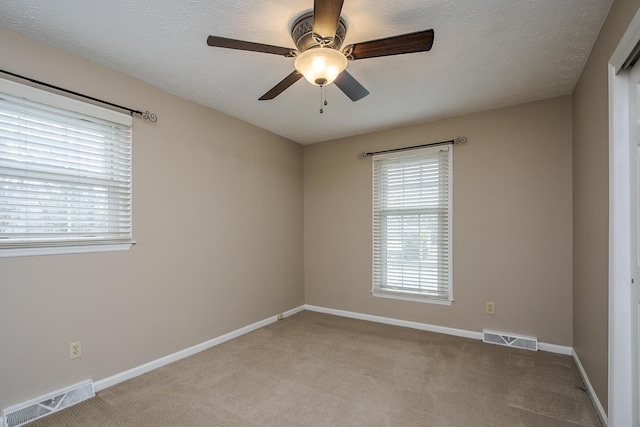 spare room with light carpet, visible vents, a textured ceiling, and baseboards