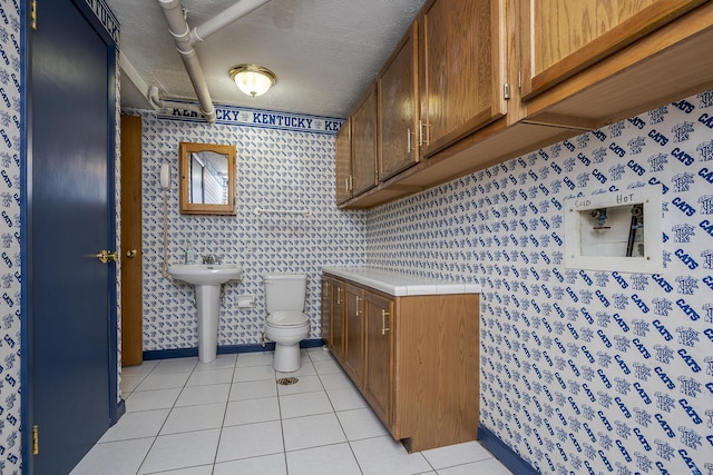 bathroom with tile patterned flooring, toilet, wallpapered walls, and a textured ceiling