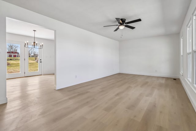 spare room with baseboards, light wood-style floors, and ceiling fan with notable chandelier