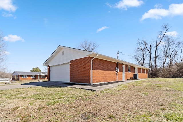 view of side of property featuring central air condition unit, driveway, a yard, a garage, and brick siding