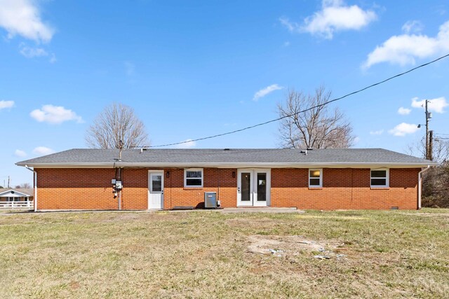 rear view of house with brick siding, a lawn, french doors, and roof with shingles