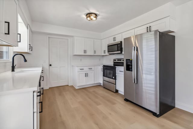 kitchen with light wood-type flooring, light countertops, appliances with stainless steel finishes, white cabinets, and a sink