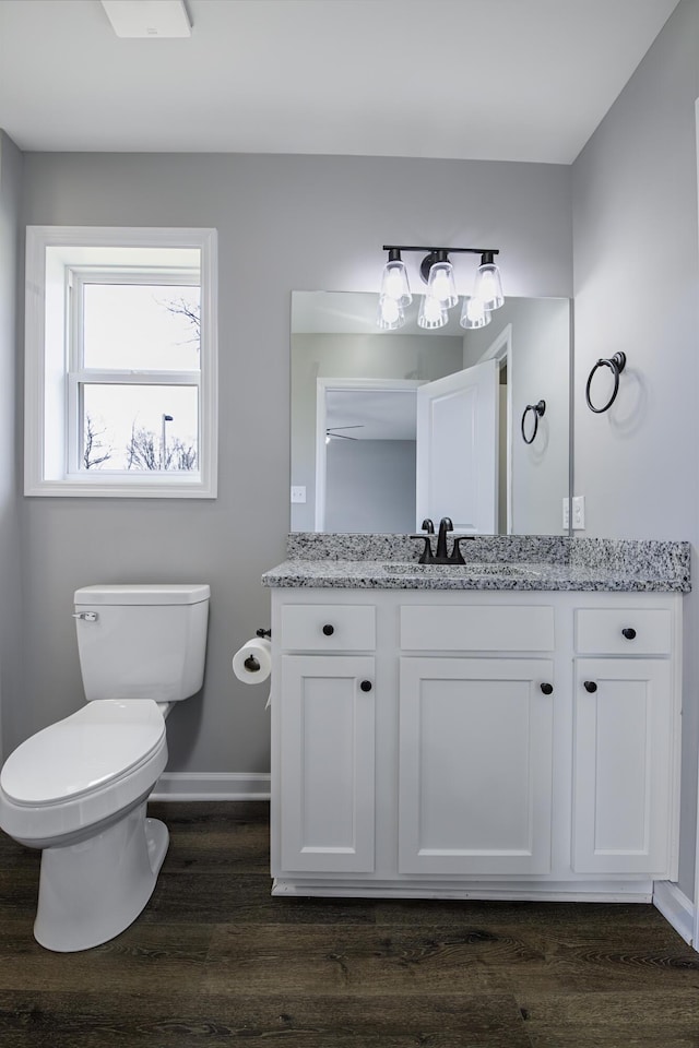 bathroom with toilet, vanity, baseboards, and wood finished floors