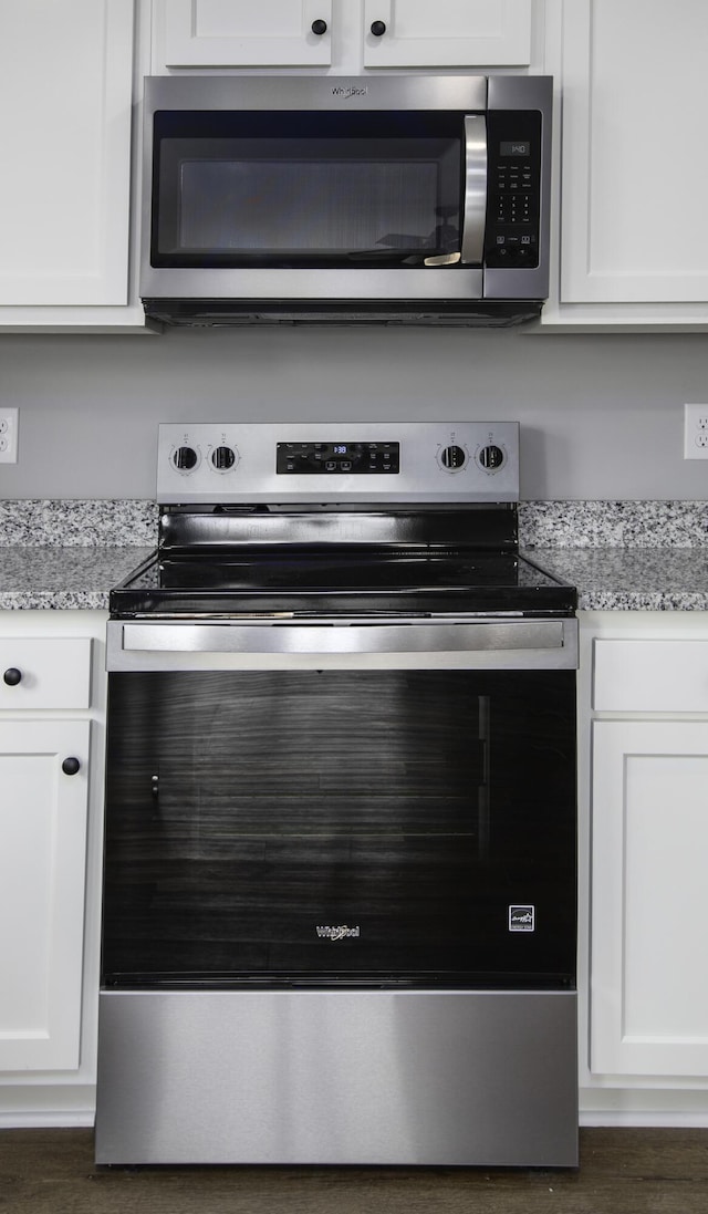 room details featuring stainless steel appliances, light stone countertops, and white cabinets