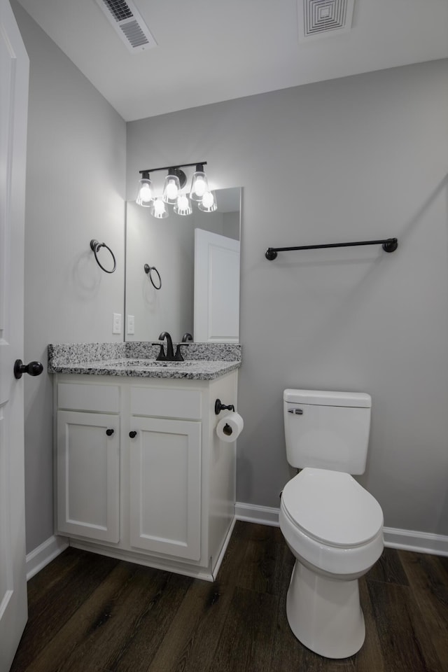 half bathroom featuring toilet, wood finished floors, visible vents, and baseboards