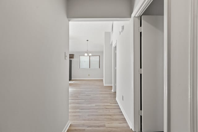 corridor with light wood-style flooring, an inviting chandelier, and baseboards