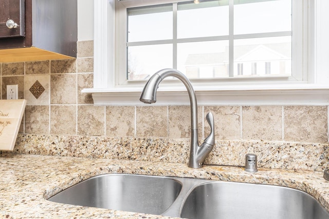 interior details featuring a sink, light stone countertops, tasteful backsplash, and dark brown cabinetry