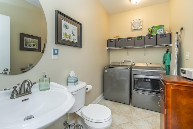 half bath with tile patterned flooring, baseboards, toilet, separate washer and dryer, and a sink