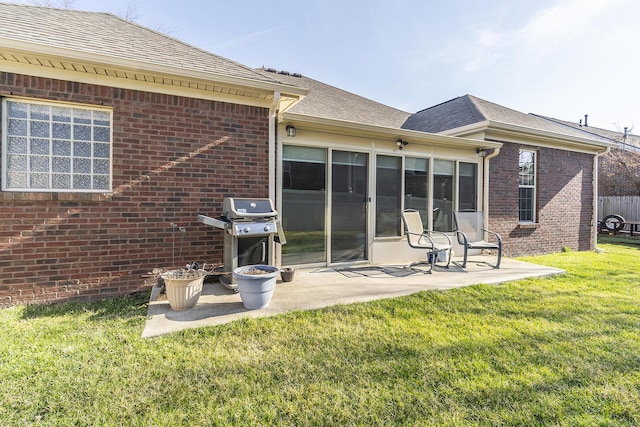 rear view of house with brick siding, roof with shingles, a lawn, and a patio area