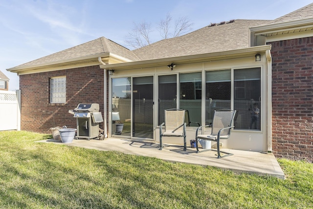 rear view of property featuring brick siding, a lawn, a shingled roof, and a patio