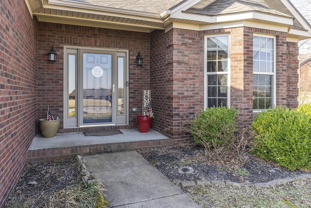 entrance to property featuring brick siding and roof with shingles