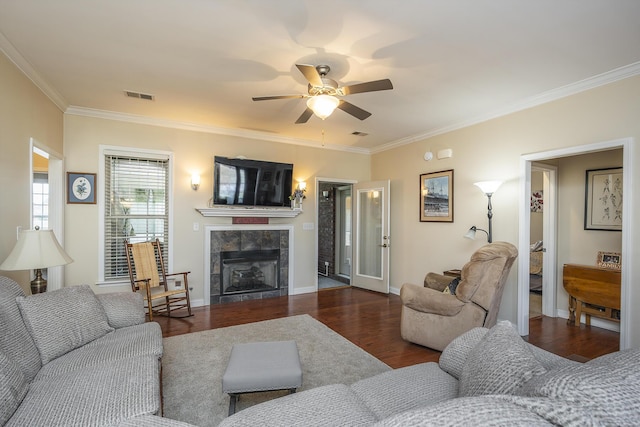 living room featuring visible vents, crown molding, baseboards, a tiled fireplace, and wood finished floors